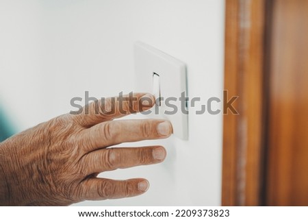 Close up of old hand senior woman switching off or on home light. Concept of saving bills for energy and electricity. Supply reduction in winter. Environment care for mature people. Europe crisis