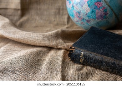 Close up the old holy bible with a blurred world globe on vintage linen sackcloth background against, copy space, Christian background, bible study, or devotional concept.