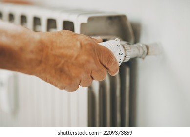 Close Up Of Old Man Hand Closing  Heating Home Thermostat For Gas Energy Saving. Concept Of Bills And Heat Crisis Costs. People Adjusting Radiator Supply To Save Money During Winter