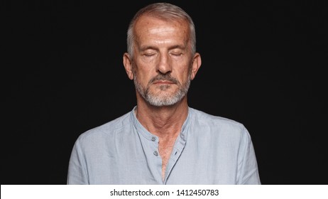 Close Up Of An Old Man With His Eyes Closed. Portrait Of A Senior Man Against Black Background.