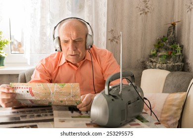 Close Up Old Man Listening From Radio With Headset While Reading Tabloid At The Living Room Area.