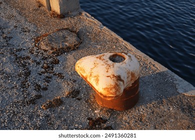 Close up of old rusted peach mooring bollard on the stone pier.. Navy sea water. Noblessner, Tallinn, Estonia. July 2024. - Powered by Shutterstock