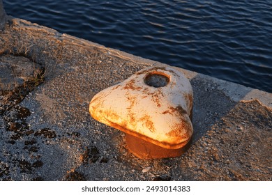 Close up of old rusted peach mooring bollard on the stone pier.. Navy sea water. Noblessner, Tallinn, Estonia. July 2024. - Powered by Shutterstock