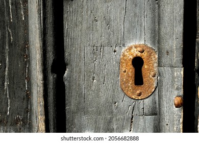 A close up of an old rusty metal keyhole on an old wooden door 