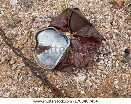 Close up of an old smashed rusty pull tab beverage can and a piece of twisted old rusty wire lying on the ground.