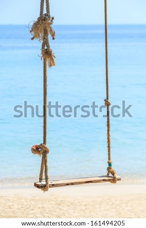 Close up old and weathered rope and wooden swing by the beach and blue sea
