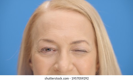 Close Up Old Woman Eyes In Front Of Blue Background Wink. Close Up Eyes Of The Concept.