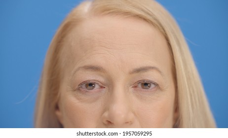 Close Up Old Woman Eyes In Front Of Blue Background Wink. Close Up Eyes Of The Concept.