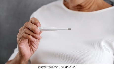 Close up of old woman hand holding thermometer at home, Flu asia fmale holding a digital thermometer when measures the temperature, People get fever, infection from virus check body temperature - Powered by Shutterstock