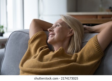 Close up older peaceful woman put hands behind head rest leaned on sofa cushions smile looks into distance, take break at home, enjoy fresh conditioned air inside. Hotel accommodation, relax concept - Shutterstock ID 2174173025