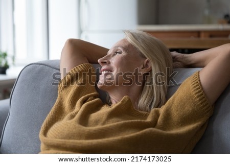 Close up older peaceful woman put hands behind head rest leaned on sofa cushions smile looks into distance, take break at home, enjoy fresh conditioned air inside. Hotel accommodation, relax concept