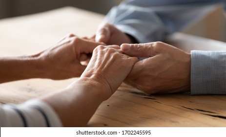 Close up older spouses holding hands on wooden table, loving caring mature man comforting senior wife, family expressing empathy and understanding, trusted relationship in marriage