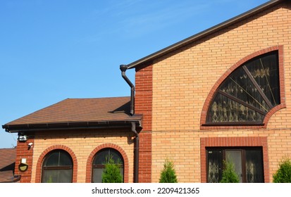 Close Up On Asphalt Shingles Brick House Rooftop With Rain Gutter Pipeline System. 