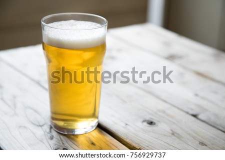 Close up on a backlit beer glass filled with a pale blonde ale, on a wood picnic table at a craft brewery