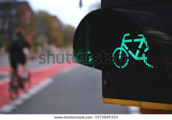 close up on bicycle\
traffic light in yellow housing showing green light at an urban\
intersection with moving cyclist in background - selective focus\
with excessive blur