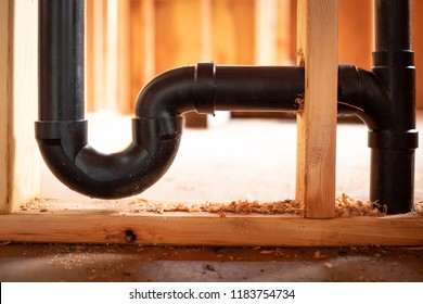 Close up on a black ABS plastic U bend trap, for a residential plumbing and sewer system, in wood wall studs