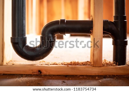 Close up on a black ABS plastic U bend trap, for a residential plumbing and sewer system, in wood wall studs