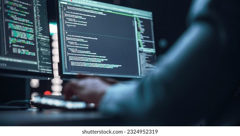 Close Up on Black Male Hands Typing on a Desktop Computer Keyboard In Dark Network Security Office. Professional Programmer Writing Code Displayed on Two Monitor Screens. High Tech Developing Concept.