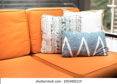 Close Up On Blue And White Pattern Throw Pillows On An Outdoor Patio Chair, With An Orange Couch Cushion Bench, On A Backyard Deck