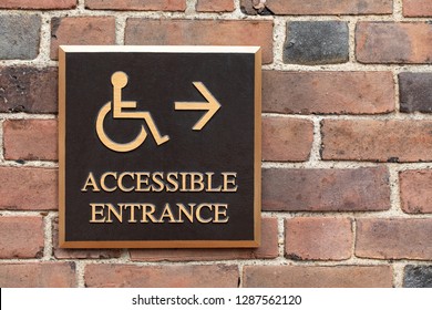 Close up on a bronze wheelchair and handicapped accessible entrance sign, on a brick wall
