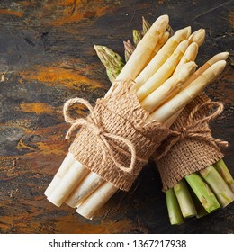 Close up on a bundle of fresh white asparagus spears resting over a second green one beneath tied with string and hessian on a rusty metal background in square format