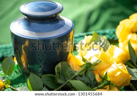 Close up on a burial urn with yellow roses, in a bright funeral scene, with space for text on the right
