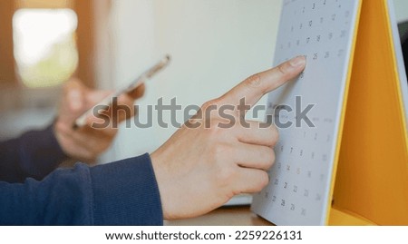 close up on businessman hand using pen to writing schedule on calendar 2023 to make appointment meeting or manage timetable each day at house for work from home concept	