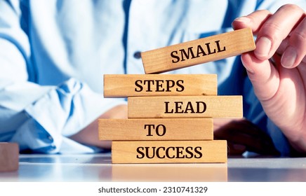 Close up on businessman holding a wooden block with a "Small steps lead to success" message - Shutterstock ID 2310741329