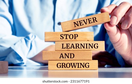 Close up on businessman holding a wooden block with a "Never stop learning and growing" message - Shutterstock ID 2311677191
