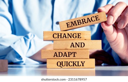 Close up on businessman holding a wooden block with a "Embrace change and adapt quickly" message - Shutterstock ID 2311678957