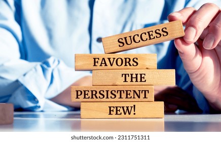 Close up on businessman holding a wooden block with a "Success favors the persistent few" message - Shutterstock ID 2311751311