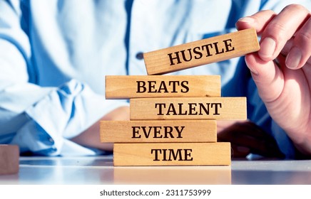 Close up on businessman holding a wooden block with a "Hustle beats talent every time" message - Shutterstock ID 2311753999