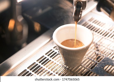 Close Up On A Coffee Cup Filled By The Coffee Machine Of A Bar. No People Are Visible. Low Key Image.