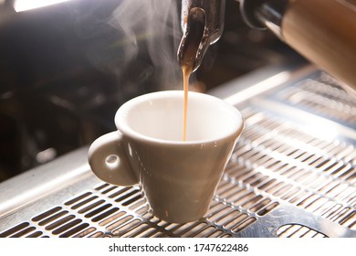 Close Up On A Coffee Cup Filled By The Coffee Machine Of A Bar. No People Are Visible. Low Key Image.