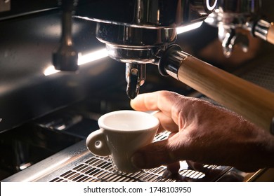 Close Up On A Coffee Cup Filled By The Coffee Machine Of A Bar. No People Are Visible. Low Key Image.