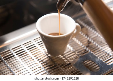 Close Up On A Coffee Cup Filled By The Coffee Machine Of A Bar. No People Are Visible. Low Key Image.