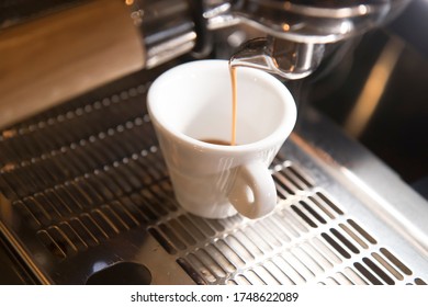 Close Up On A Coffee Cup Filled By The Coffee Machine Of A Bar. No People Are Visible. Low Key Image.