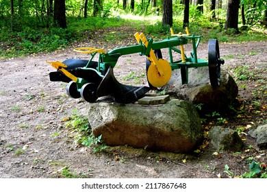 A close up on a colorful metal device that was used by farmers to plough the field in the past and now used as a decoration attached to a big stone, boulder or rock seen in the middle of a forest