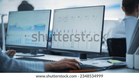Close Up on Computer Monitors of Male Financial Data Analyst Using Laptop And Studying Information And Graphs On Big Digital Screen In Monitoring Office. Man Working For Big Consulting Firm
