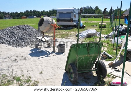  Close up on concrete mixer, cement mortar mixing with construction wheel barrow on house construction site.