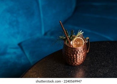 Close up on a copper cup with Moscow Mule cocktail, fresh mint as decoration and a white and orange, tiki fresh cocktail served in a bar
