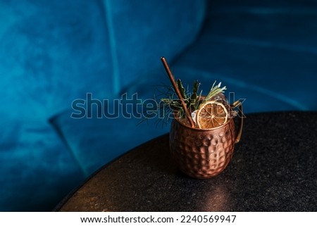 Close up on a copper cup with Moscow Mule cocktail, fresh mint as decoration and a white and orange, tiki fresh cocktail served in a bar