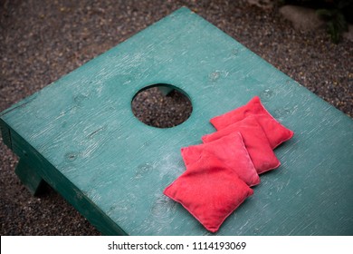 Close up on a Corn Hole game set with red bean bags on a green wood board, and space for text