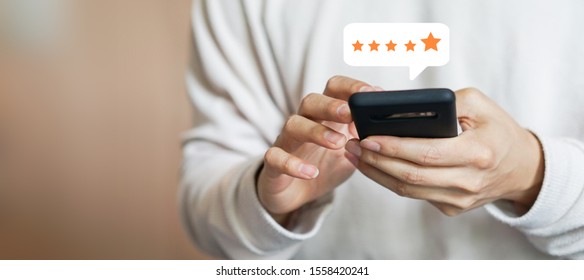 Nahaufnahme auf der Hand des Kunden, indem er auf dem Smartphone-Bildschirm mit goldenem Fünf-Sterne-Feedback-Symbol auf der Bewertung drückt, und auf der Presseebene hervorragender Rang für die beste Punktzahl zur Überprüfung des Dienstes, des Geschäftskonzepts
