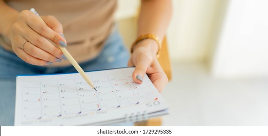 Näherung in der Hand von Angestellten mit Stift zum Schreiben des Terminkalenders im Kalender, um die Terminabsprache zu machen oder den Zeitplan für die Arbeit von zu Hause aus zu verwalten	