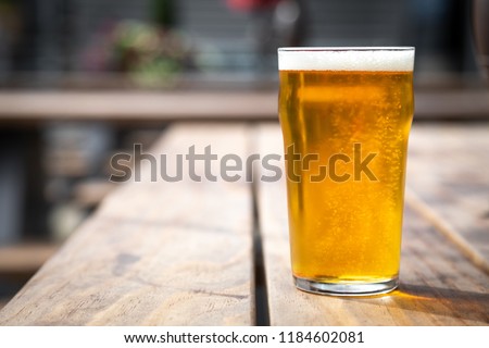Close up on an English pint glass of lager beer, on an outdoor wooden table, with space for text on the left