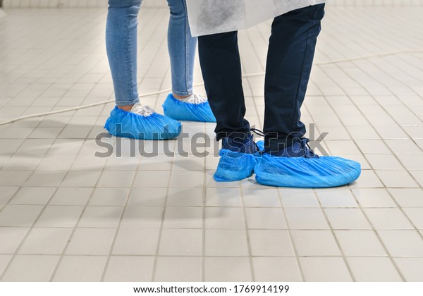 Close up on feet of unknown man and woman\
wearing overshoes - Blue medical shoe covers for protection on\
floor in hospital - Medical antibacterial plastic disposable pull\
on slippers hygiene\
standard