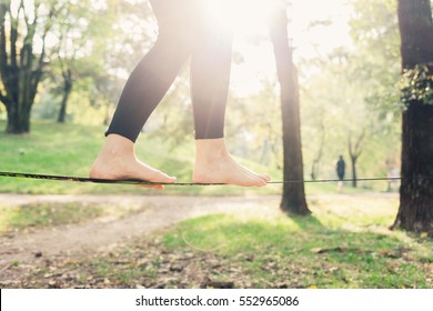 Close Up On Feet Walking On Tightrope Or Slackline Outdoor In A City Park In Back Light - Slacklining, Balance, Training Concept 
