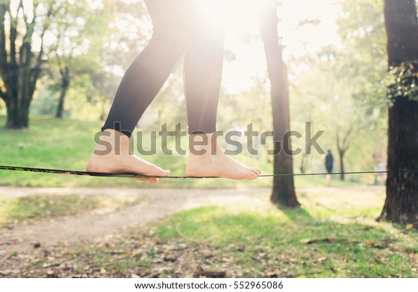 Close up on feet walking on tightrope or slackline\
outdoor in a city park in back light - slacklining, balance,\
training concept 