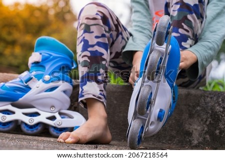 close up on foot of asian kids on the floor taking off or putting on the rollerblade inline skates tying laces while sitting on footpath at park in day fun freedom motion and youth concept
